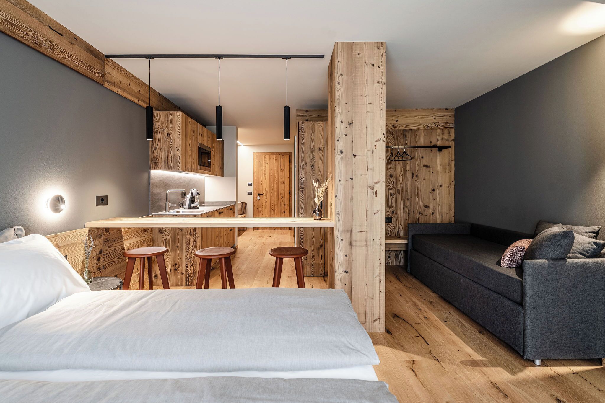 Une chambre moderne avec un grand lit, un canapé et un petit coin cuisine équipé de tabourets.