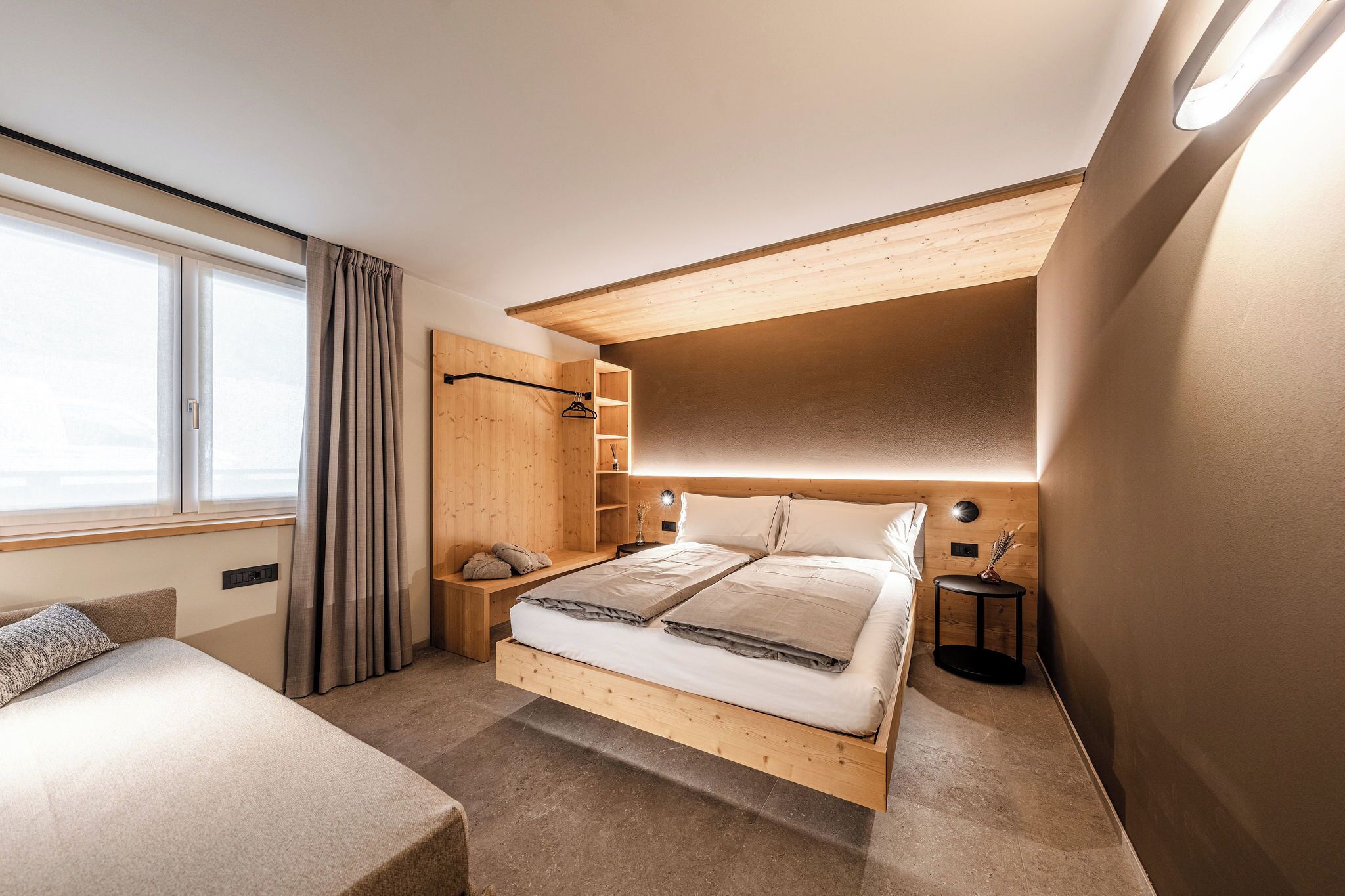Een moderne slaapkamer met een houten bed, nachtkastje, kast en een raam met gordijnen.