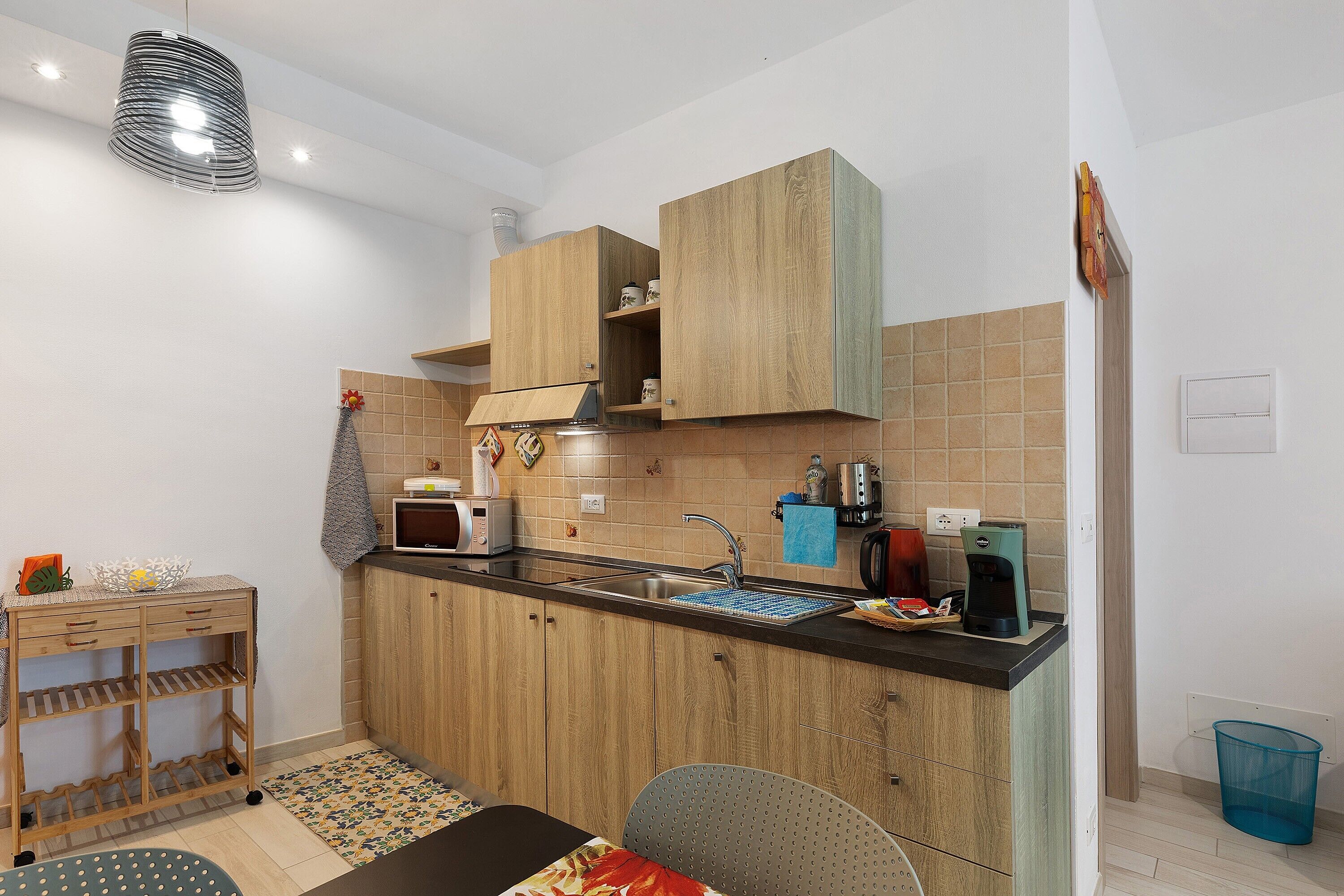 Een compacte keuken met houten kastjes, een magnetron, een koffiezetapparaat en een spoelbak.