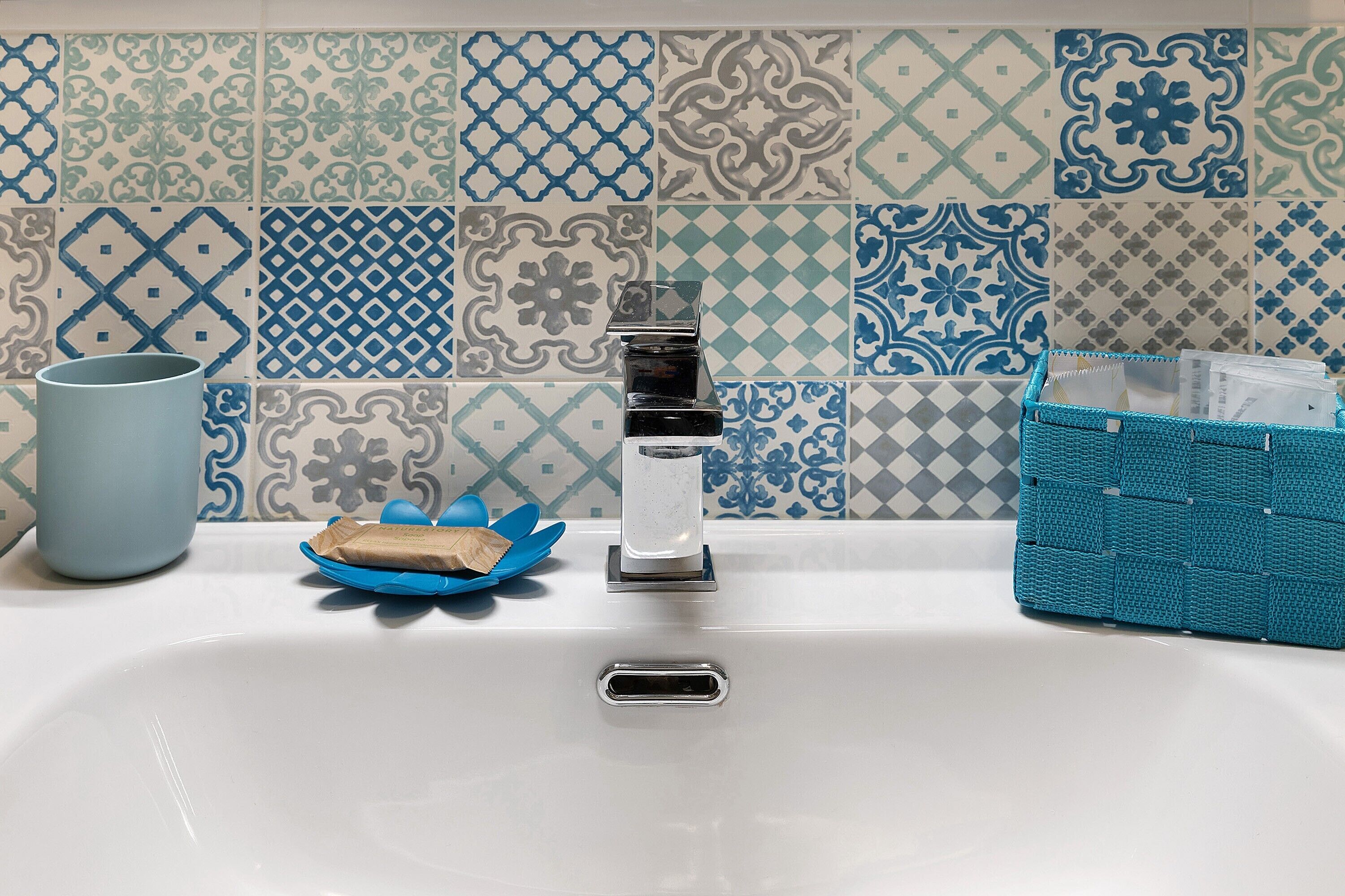 Un lavabo de salle de bain avec un robinet, un porte-savon et un panier bleu.