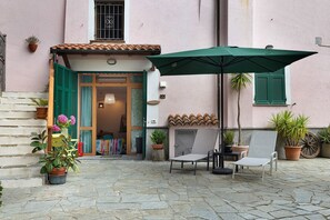 A stone-floored patio with a chair and umbrella, potted plants, and a building entrance. - Studio Apartment 'Quercia -in Caruggiu Di Via Vecchia' with Mountain View, Wi-Fi and Air Conditioning (orco feglino)