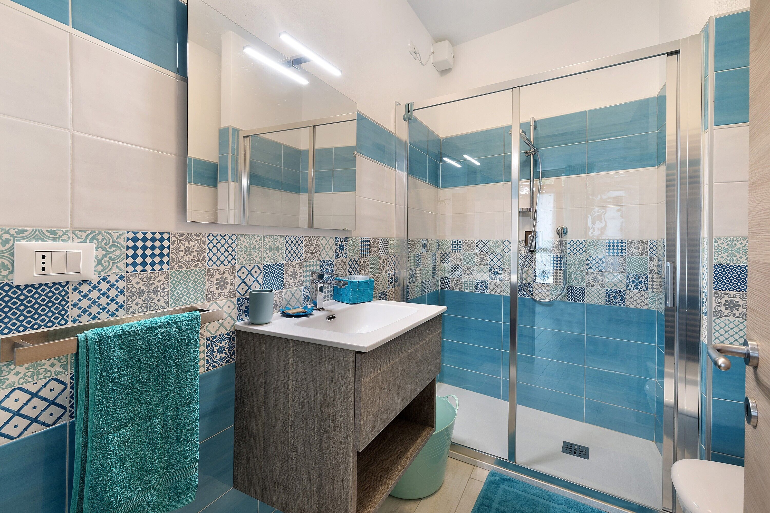 Un baño con cabina de ducha de vidrio, un lavabo con espejo y azulejos estampados en las paredes.