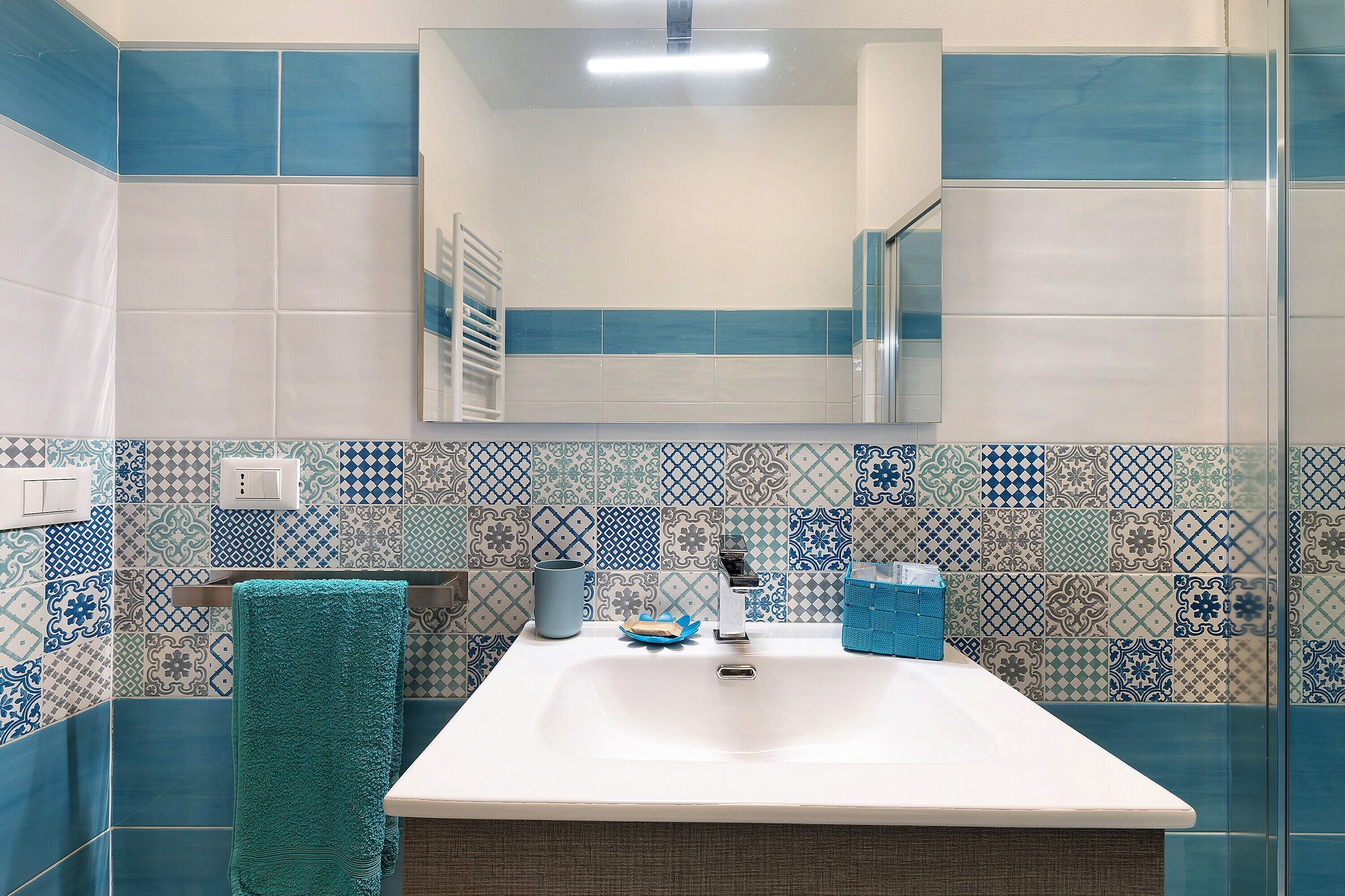 Une salle de bain avec un lavabo blanc, des carreaux bleus et blancs à motifs, un porte-serviettes et un miroir.