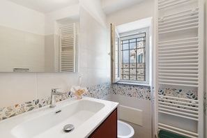 Un bagno con un lavandino bianco, uno specchio, una finestra con vista e uno spazio doccia.