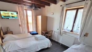Slaapkamer met twee bedden, een bureau, een stoel, een televisie en een raam met gordijnen.