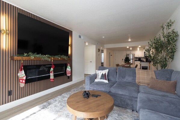 A modern living room with a large flat-screen TV, a grey sofa, a wooden coffee table, and a fireplace with stockings. - Cozy 2-bedroom Resort condo in Branson with Heated Pool and fitness Center (Branson)