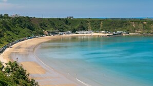 A coastal beach with a curved shoreline, a row of beach huts, and a lighthouse in the distance. - Hafan Nefyn - sleeps 8 guests  in 4 bedrooms (Nefyn)