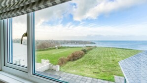 A view from a window overlooking a grassy area with a body of water and cliffs in the distance. - Hafan Nefyn - sleeps 8 guests  in 4 bedrooms (Nefyn)