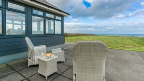 A seaside hotel room with a large window, wicker furniture, and a view of the sea. - Hafan Nefyn - sleeps 8 guests  in 4 bedrooms (Nefyn)