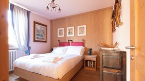 Een slaapkamer met een houten bed, een nachtkastje met boeken, een houten hoofdbord en een rustieke wanddecoratie.