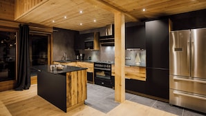 Una cocina moderna con vigas de madera, una isla central, electrodomésticos de acero inoxidable y una paleta de colores oscuros.
