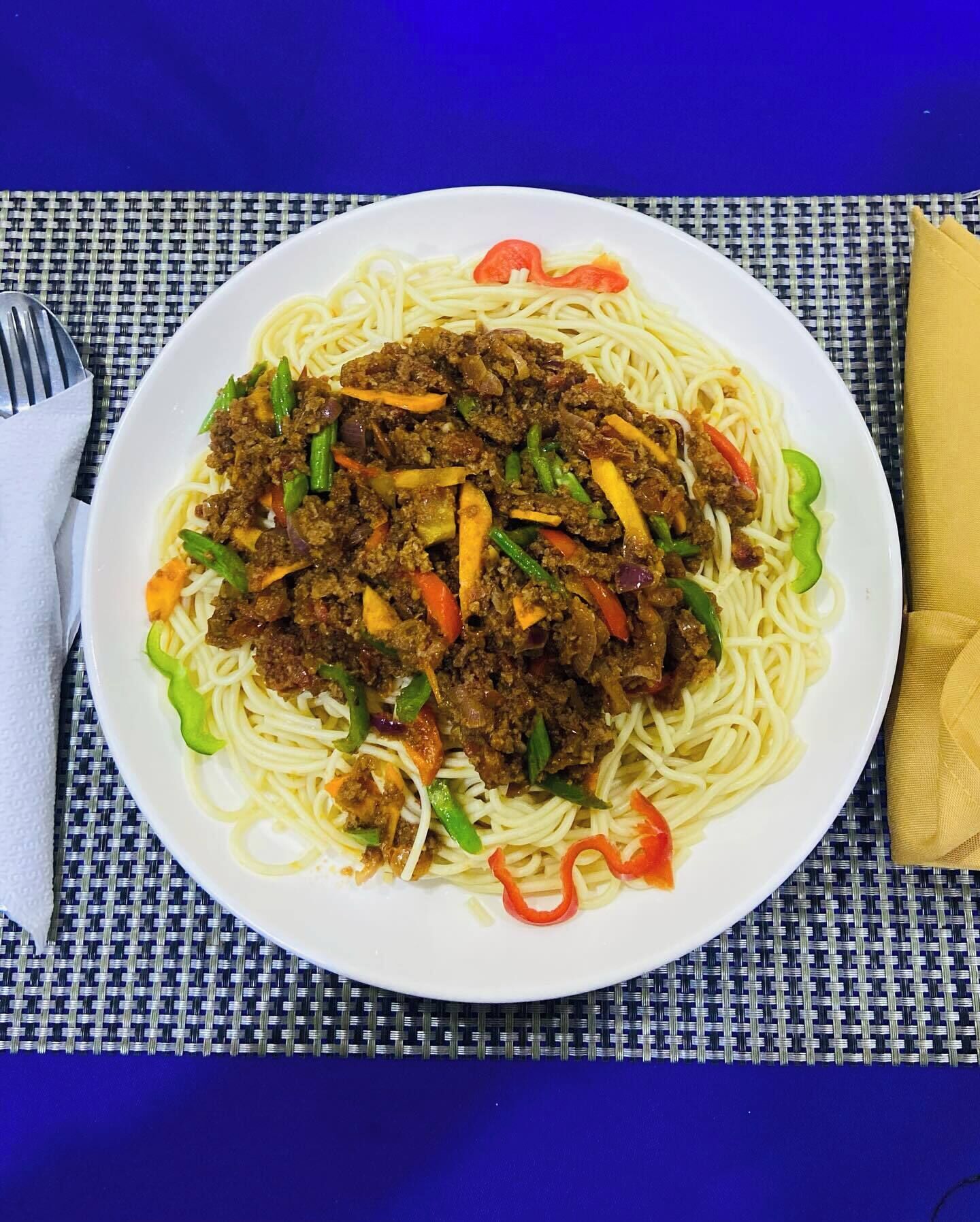 Un plato de espagueti con carne y verduras sobre un mantel azul.