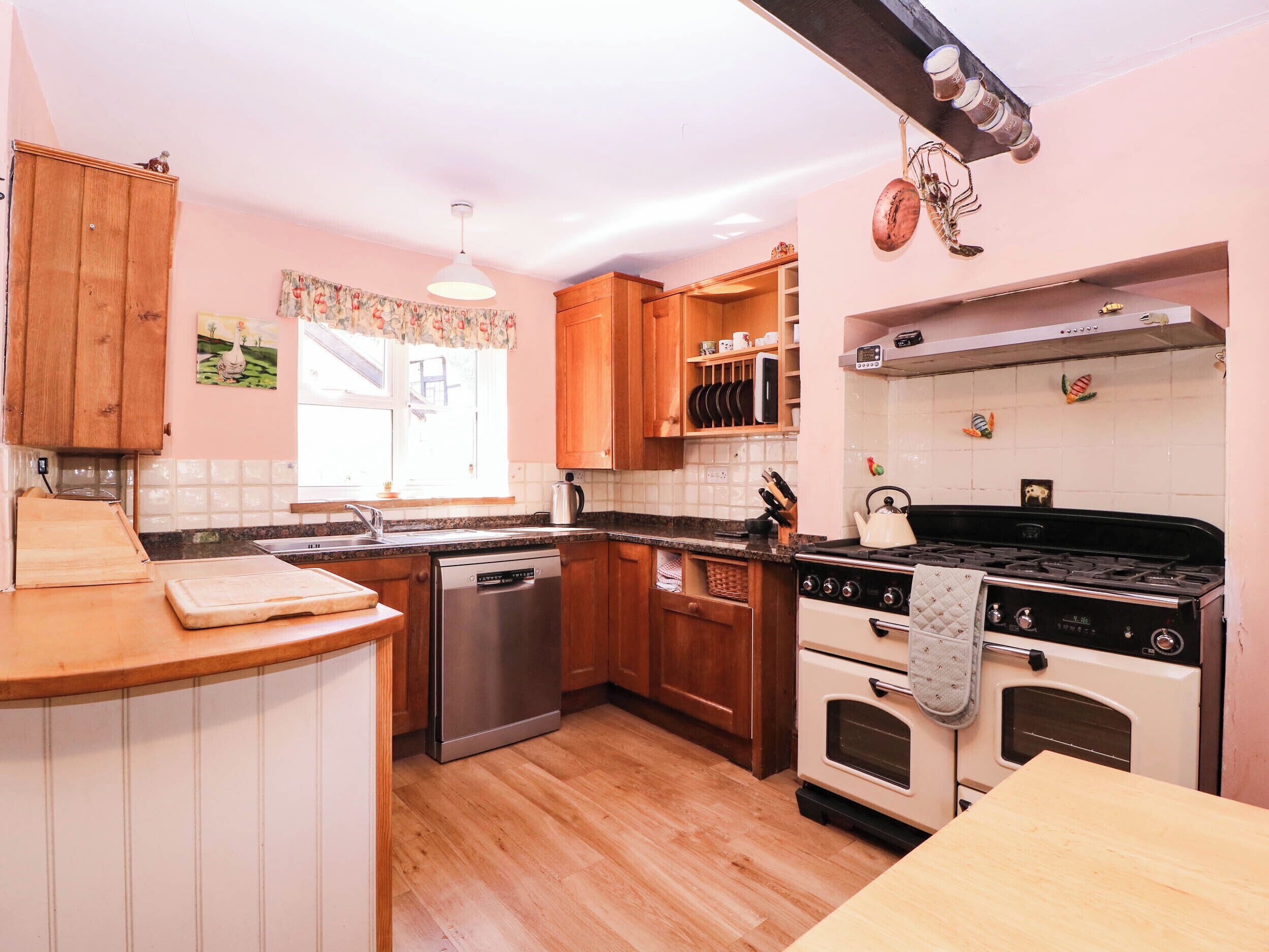 A kitchen with wooden cabinets, a dishwasher, a stove, and a window with floral curtains.