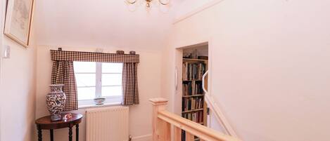 A staircase leading to a landing with a radiator, a table with a vase, and a bookshelf.