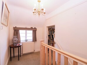 A staircase leading to a landing with a radiator, a table with a vase, and a bookshelf. - Vine Cottage (Tewkesbury)