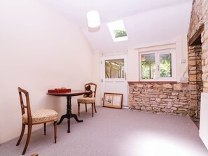 A room with a stone wall, a wooden table, two chairs, a teddy bear, a framed picture, and a skylight. - Vine Cottage (Tewkesbury)