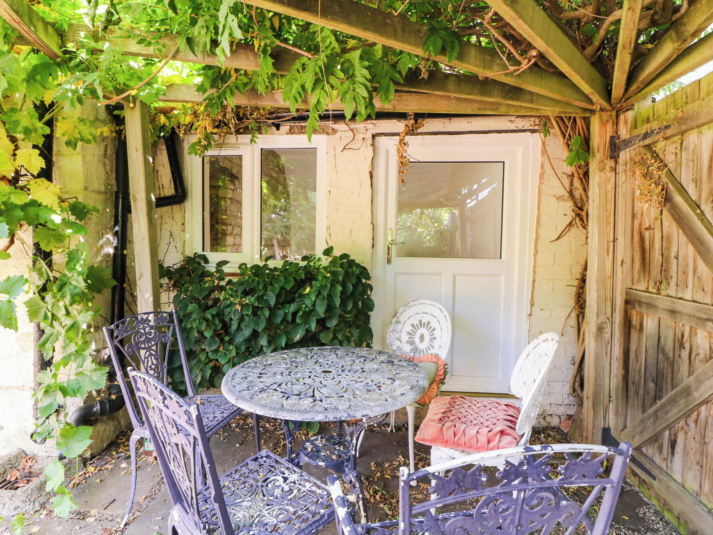 A covered outdoor seating area with a table and chairs, a door, and a wooden fence.