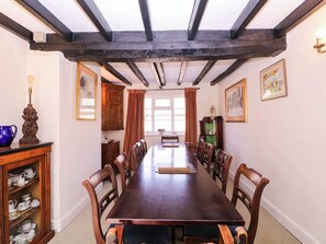 Una sala da pranzo con un lungo tavolo di legno, sedie, una credenza con porcellane e una finestra con tende.
