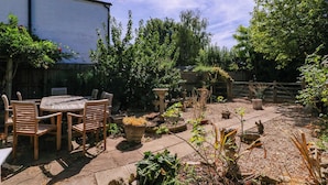 A patio area with a round table and chairs, surrounded by potted plants and a gravel path. - Vine Cottage (Tewkesbury)