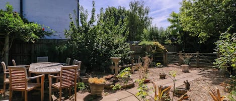 Un patio con una mesa redonda y sillas, rodeado de plantas en macetas y un sendero de grava.