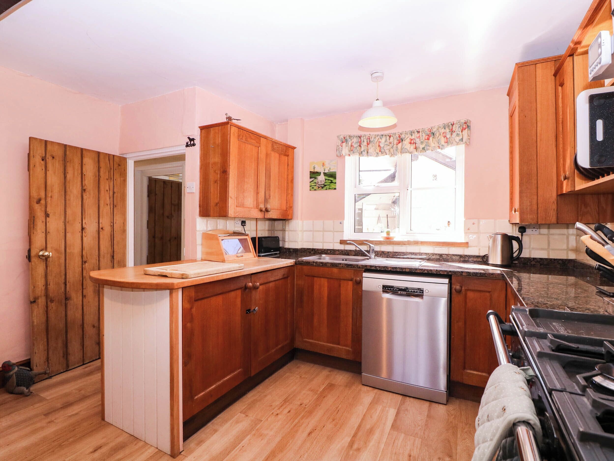 A kitchen with wooden cabinets, a built-in dishwasher, a countertop with a toaster, and a window with a view.