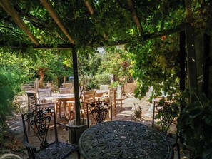 An outdoor patio with wooden tables and chairs, surrounded by greenery and a pergola. - Vine Cottage (Tewkesbury)