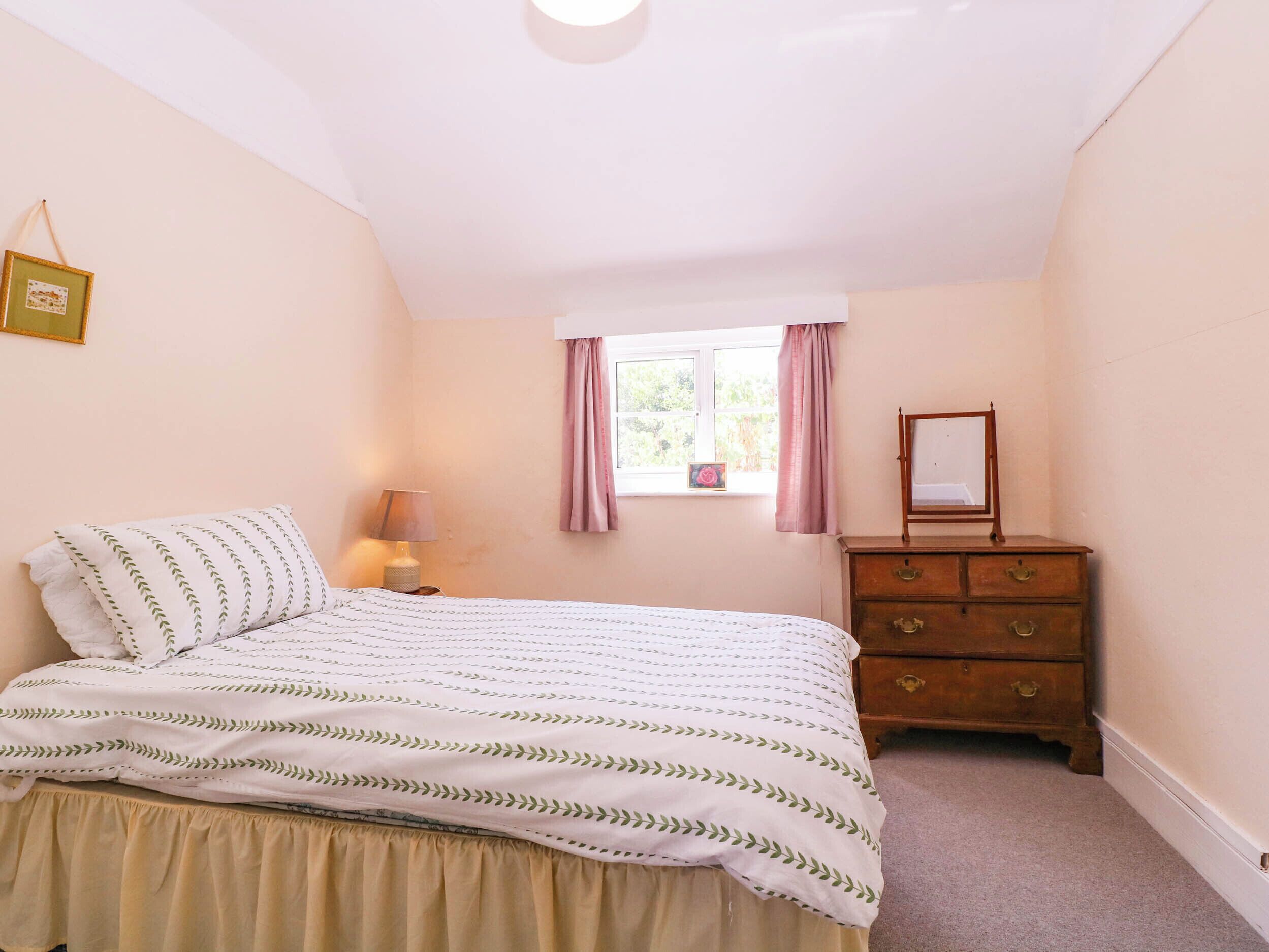 A bedroom with a bed, a dresser, a window with curtains, and a picture frame on the wall.