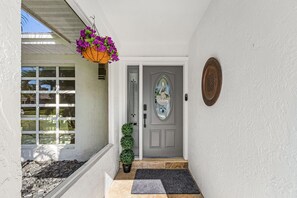 A house entrance with a grey door, a welcome mat, a potted plant, and a hanging flower basket. - Beautiful house with Pool & Game Room near Beaches in delightful Bonita Springs (Bonita Springs)
