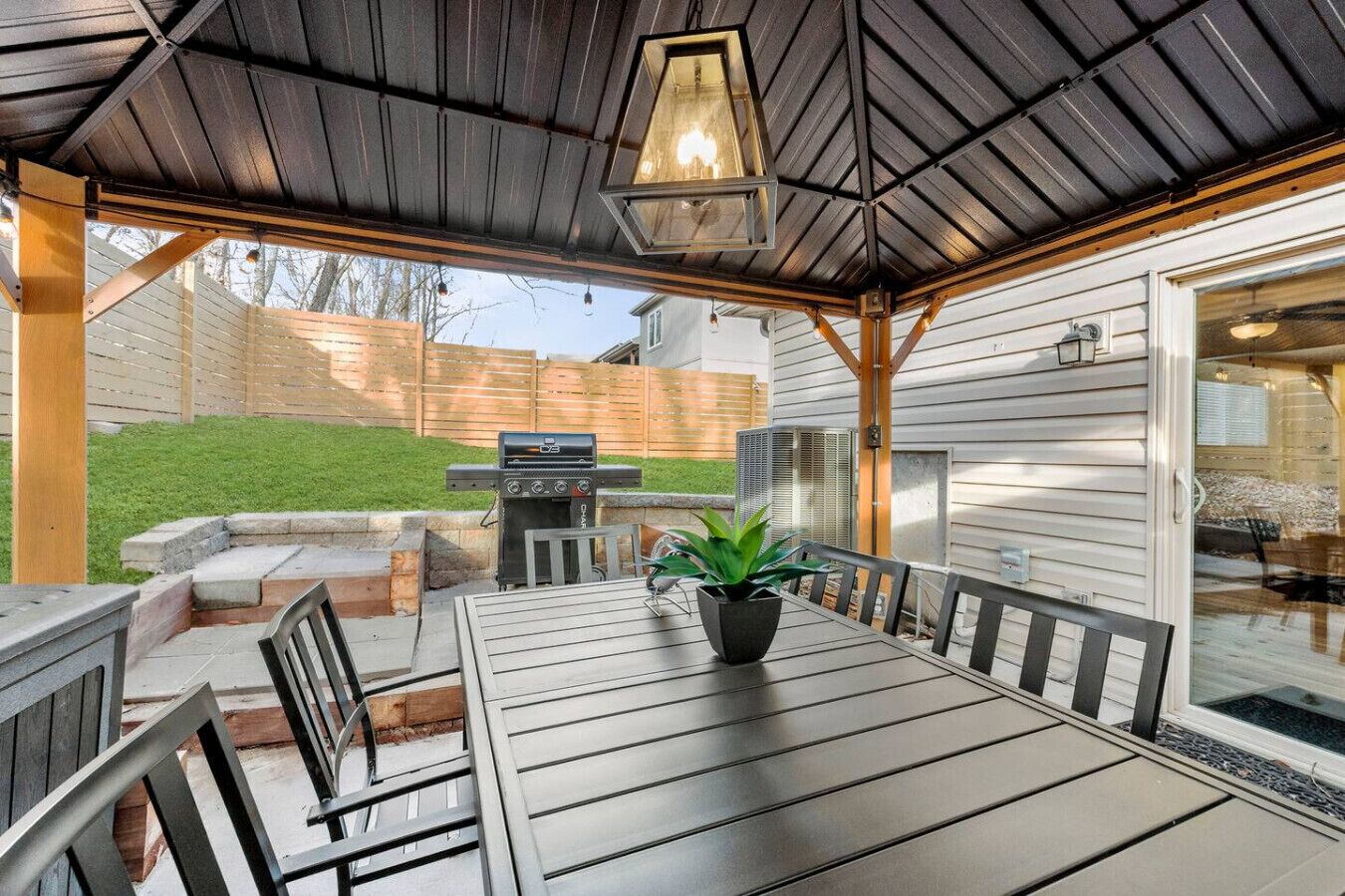 Eine Terrasse im Freien mit Tisch, Stühlen, einem Grill und einem Blumentopf.