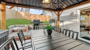 An outdoor patio with a table and chairs, a grill, and a potted plant.