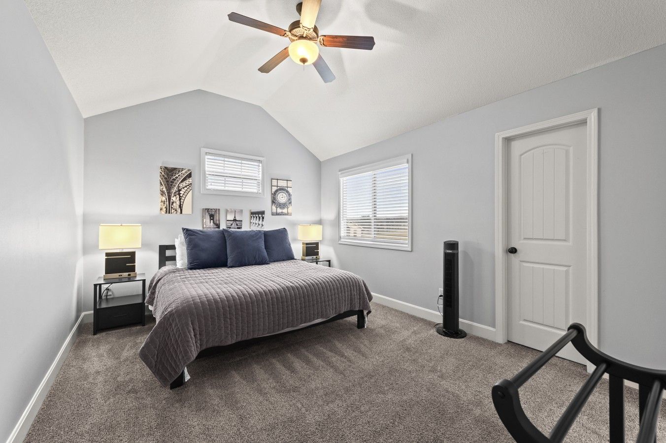 Une chambre à coucher avec un lit, des tables de chevet, un ventilateur de plafond et une porte.
