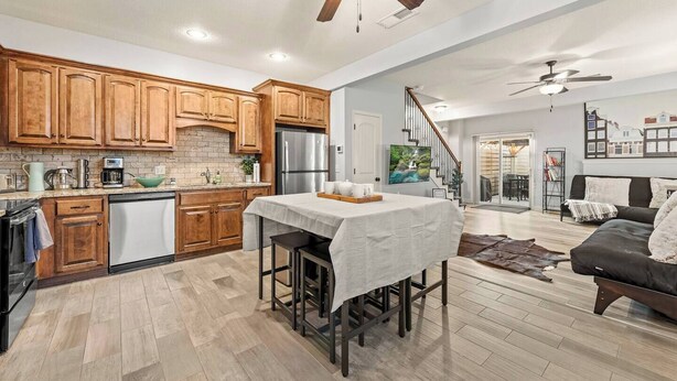 A modern kitchen with wooden cabinets, a stainless steel refrigerator, and a dining area with a table and chairs.
