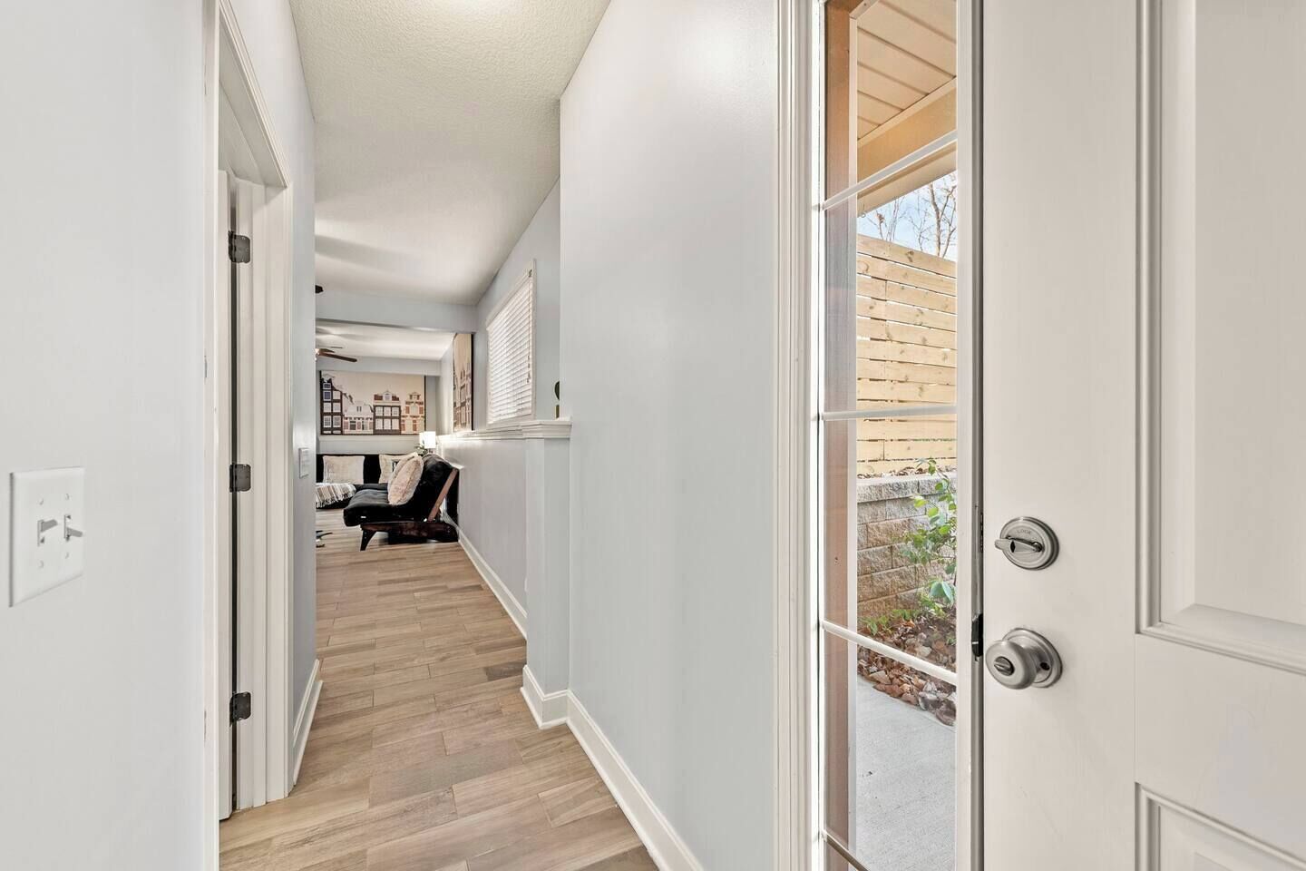 Un couloir doté d’un plancher en bois, de murs blancs et d’une porte donnant sur l’extérieur.