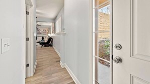 A hallway with a wooden floor, white walls, and a door leading outside.