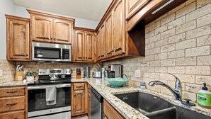 A kitchen with wooden cabinets, stainless steel appliances, a granite countertop, and a brick backsplash.