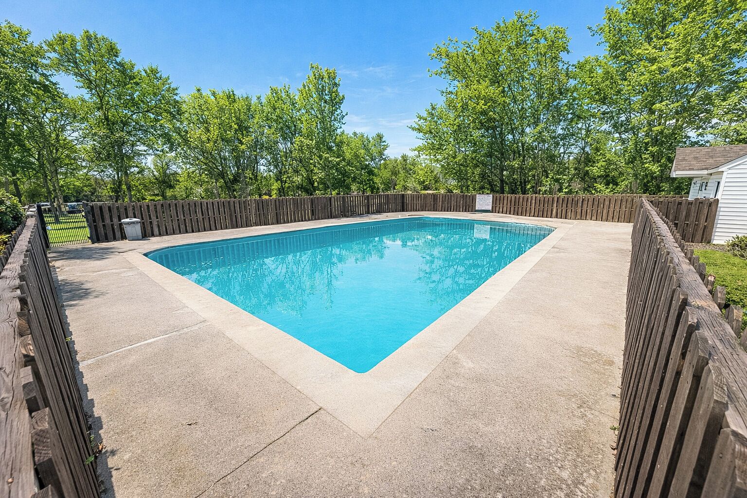 A rectangular swimming pool with a wooden deck and a wooden fence surrounding it.
