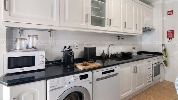 Een keuken met witte kasten, een magnetron, een koffiezetapparaat en een wasmachine.