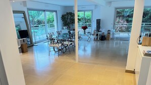 A spacious living area with a glass dining table and chairs, a large potted plant, and a view of a balcony with a railing. - Beautiful, large, bright house! 12 minutes from Paris centre.... (Deuil-la-Barre)