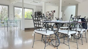 Ruime eethoek met een hoge plafond, grote ramen en een moderne keuken op de achtergrond.