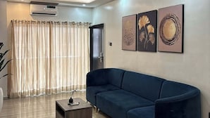 A modern living room with a dark blue sofa, a wooden coffee table, and a large window with sheer curtains. - Icempire Signature (Lagos)
