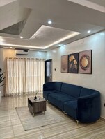 Uma sala de estar moderna com um sofá azul escuro, uma mesa de centro de madeira e uma janela grande com cortinas leves.
