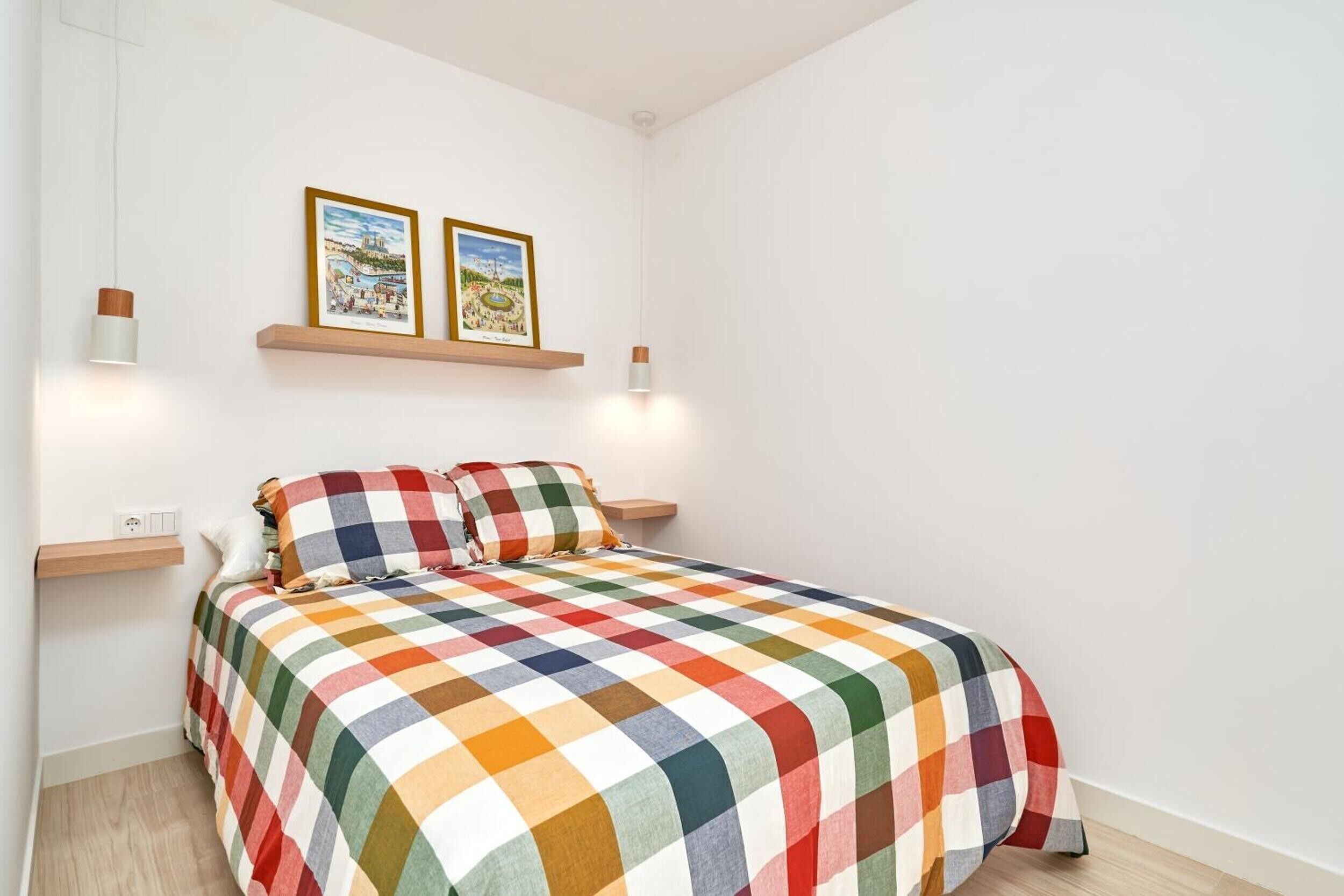 Un dormitorio con una cama, dos lámparas de pared y dos cuadros enmarcados sobre la cama.