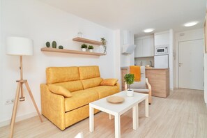 A modern living room with a sofa, a coffee table, a lamp, and a kitchen area with cabinets and a microwave. - Apartment 'Abril' with Sea View (Bremen)