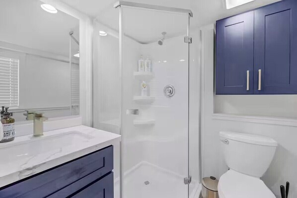 Une salle de bain moderne avec une douche à parois de verre, des accessoires blancs et des meubles bleu foncé.