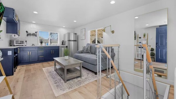 A modern kitchen with dark blue cabinets, a grey sofa, and a staircase with wooden railings.