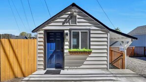 A small, single-story house with a blue door, a small porch with a planter, and a wooden fence.