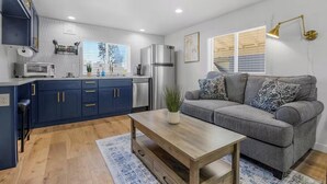 A compact living space with a kitchenette, grey sofa, wooden coffee table, and a small rug.