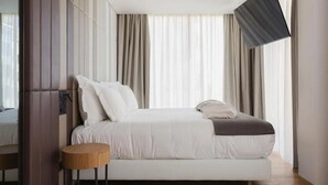 Un dormitorio moderno con una cama grande, una mesita redonda y un televisor montado en la pared.