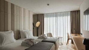 A hotel room with two beds, a desk, a chair, and a large window with curtains. - Modern Comfort & Style | Pool, Gym & Lisbon Light Show Experience (Lisboa)