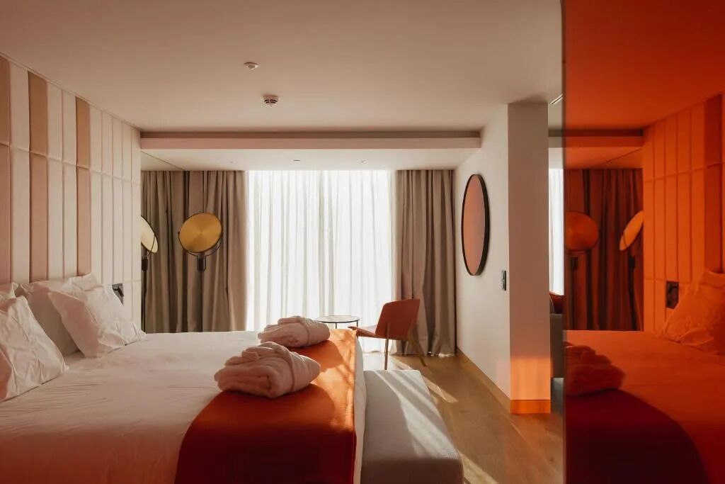 Habitación de hotel moderna con una cama grande, un escritorio y una silla. Hay cortinas en las ventanas y un espejo en la pared.